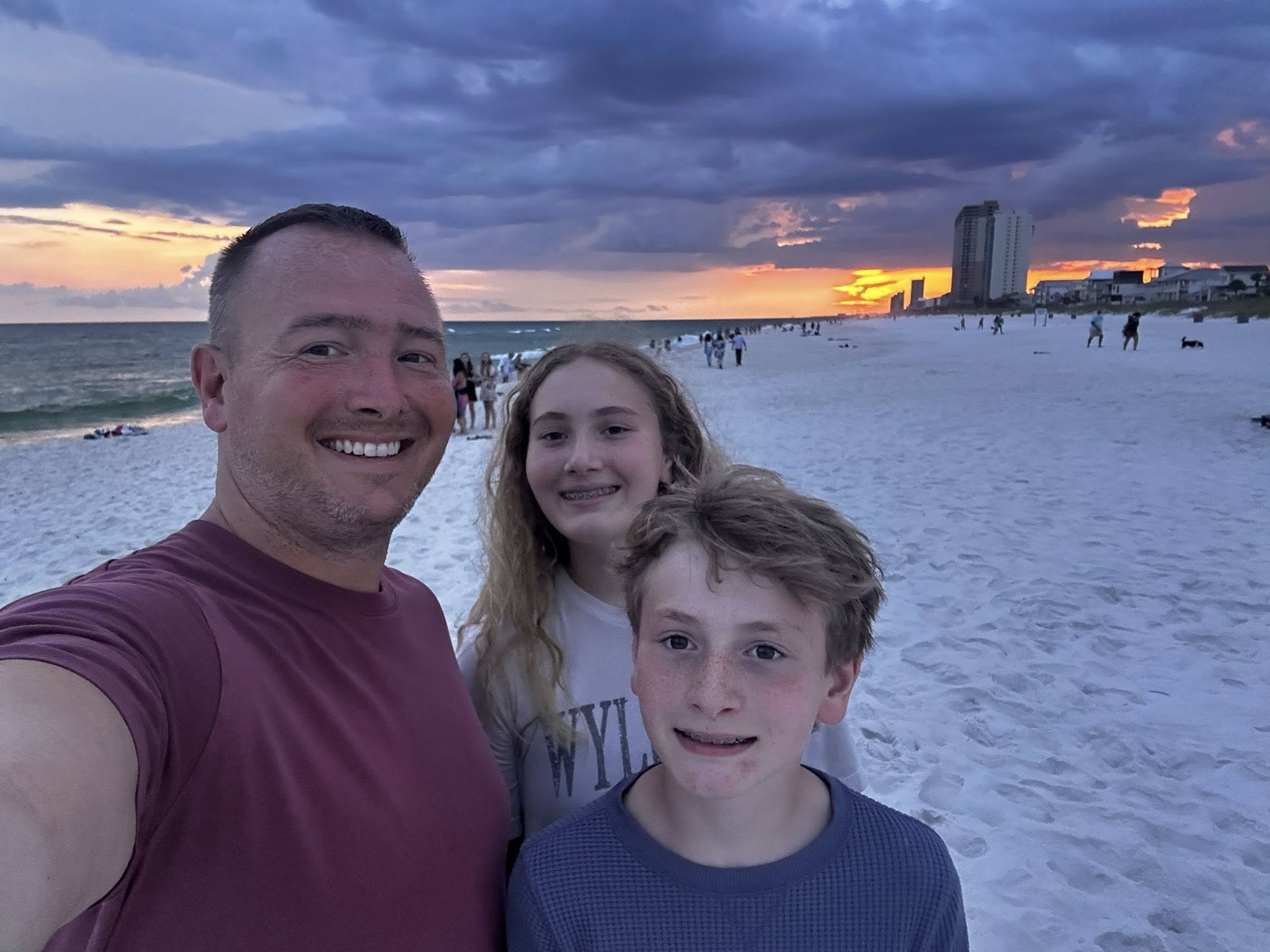 A man stands with a boy and a girl on the beach.